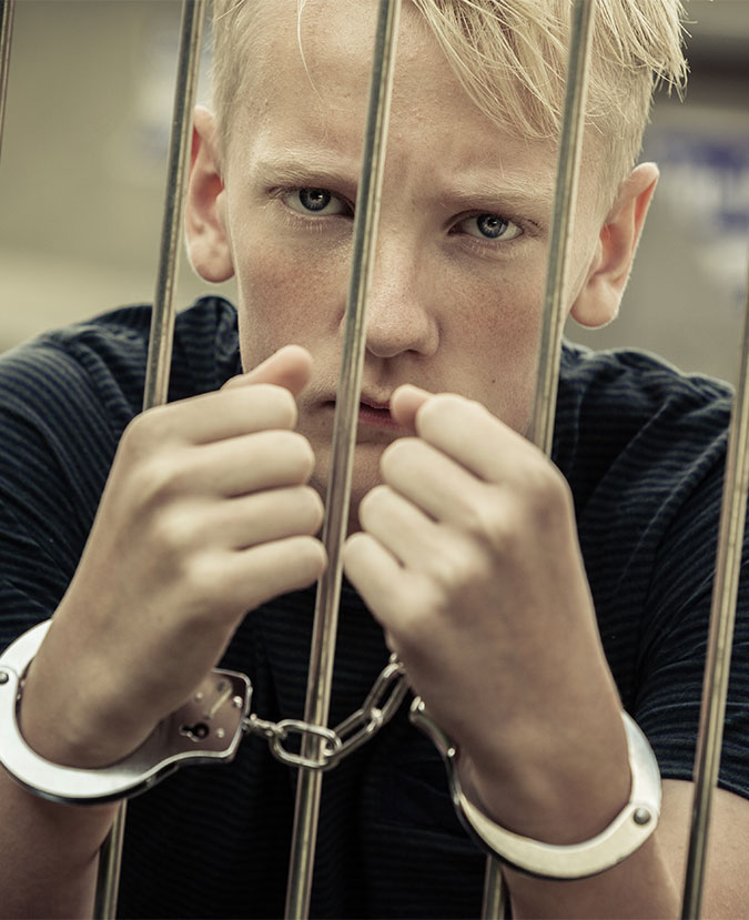 handcuffed young boy holding on the prison bars
